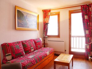 Una habitación acogedora con un sofá de madera, una mesita, un radiador y una ventana con cortinas.