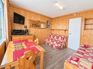A compact room with a wooden interior, a dining table with chairs, a sofa, a flat-screen TV mounted on the wall, and a door. - Cozy Studio for Couples, Ski-In/Ski-Out Access, Central Les Menuires (Les Menuires)
