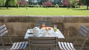 An outdoor dining area with a table set for two, including a teapot, cups, pastries, and a glass of juice. - Château du Gerfaut (Azay-le-Rideau)