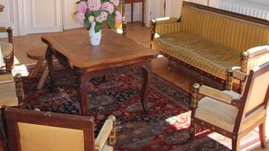 A room with a wooden table, chairs, a sofa, a patterned rug, and a large window with blue walls. - Château du Gerfaut (Azay-le-Rideau)