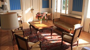 A room with a wooden sofa, a table with a vase of flowers, and a patterned rug. - Château du Gerfaut (Azay-le-Rideau)