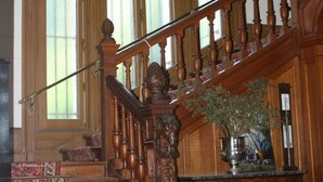 A grand staircase with ornate woodwork and red patterned carpet, leading to a landing with a vase of flowers. - Château du Gerfaut (Azay-le-Rideau)