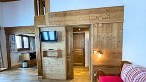 A wooden interior with a TV mounted on a wall, a bed with a red blanket, and a wooden bench.
