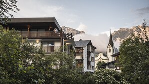 Een modern gebouw met een balkon, omringd door weelderige begroeiing en bergen op de achtergrond.