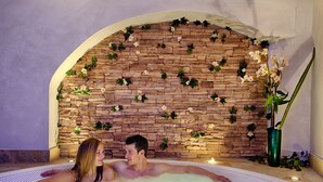 Een koppel in een jacuzzi, met een achtergrond van een stenen muur en groen.