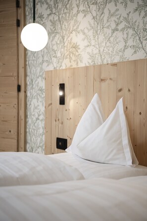 Una cama bien tendida con sábanas y almohadas blancas, cabecera de madera y pared con estampado de hojas.