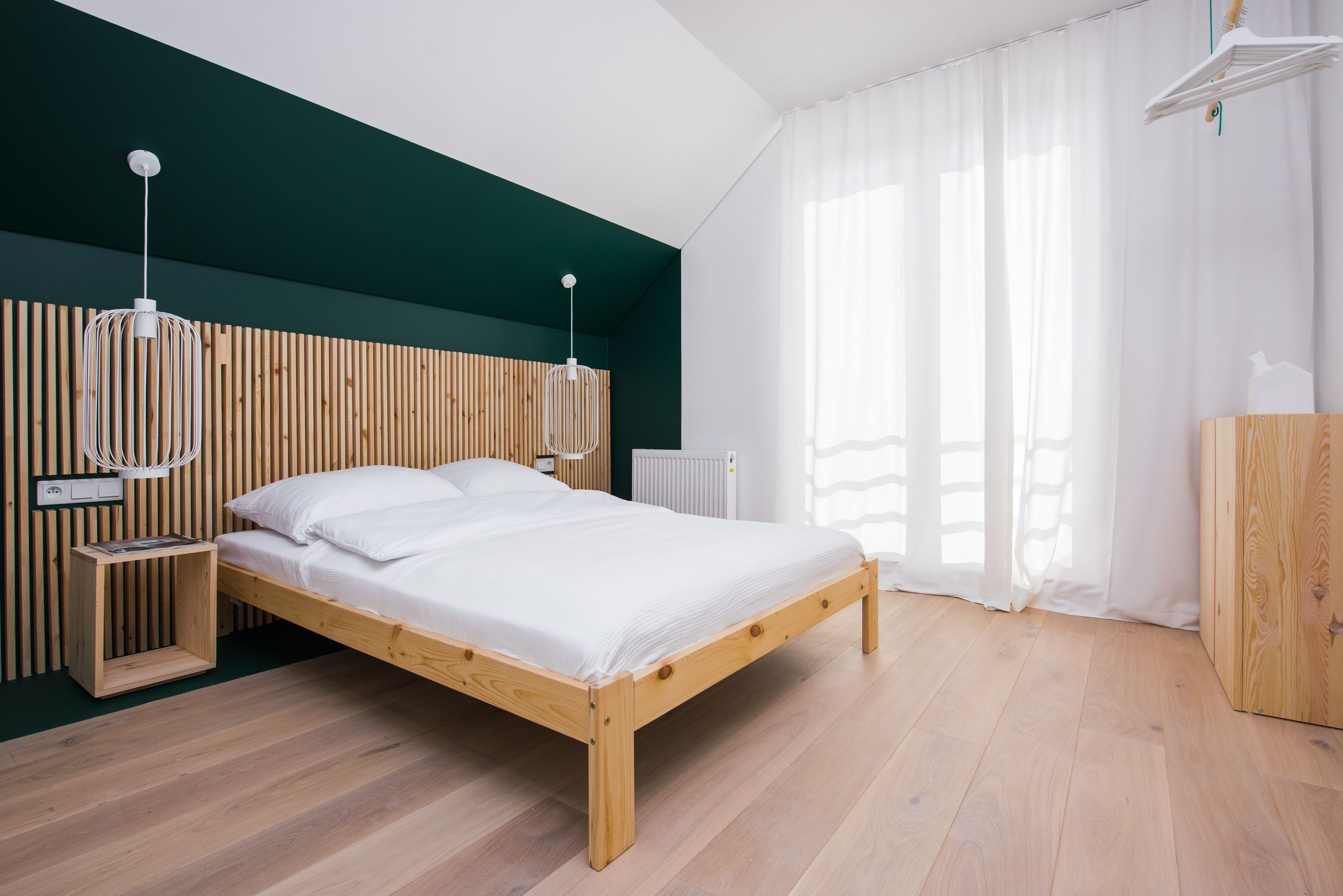 A modern bedroom with a wooden bed, white bedding, a wooden headboard, and a white pendant light.