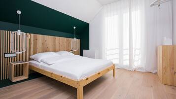 A modern bedroom with a wooden bed, white bedding, a wooden headboard, and a white pendant light.