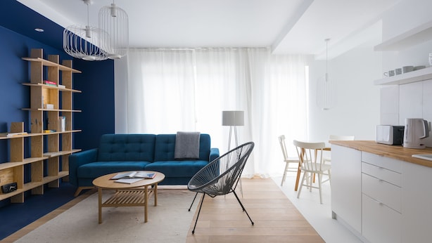 Una sala de estar moderna con un sofá azul, una silla negra, una mesa de centro de madera y una estantería.