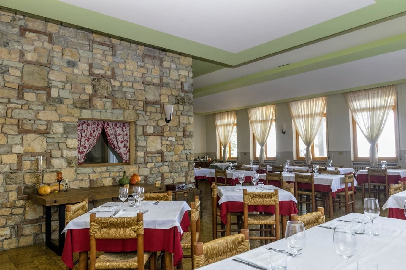 Un restaurant amb parets de pedra, diverses taules amb estovells vermells i cadires de vimet.