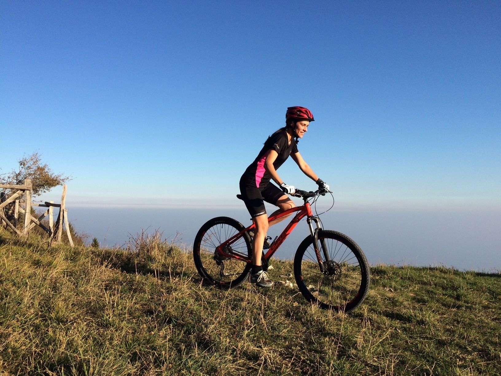 Una persona montando una bicicleta de montaña en una colina cubierta de hierba, con un cielo despejado al fondo.