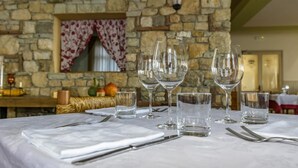 A dining table set with wine glasses and water glasses, with a stone wall and a window with red curtains in the background. - Damarco Alloggio Turistico Locanda (Schio)