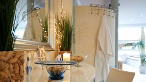 Un baño moderno con un tocador curvo, un cuenco de almendras, una toalla blanca y un espejo.