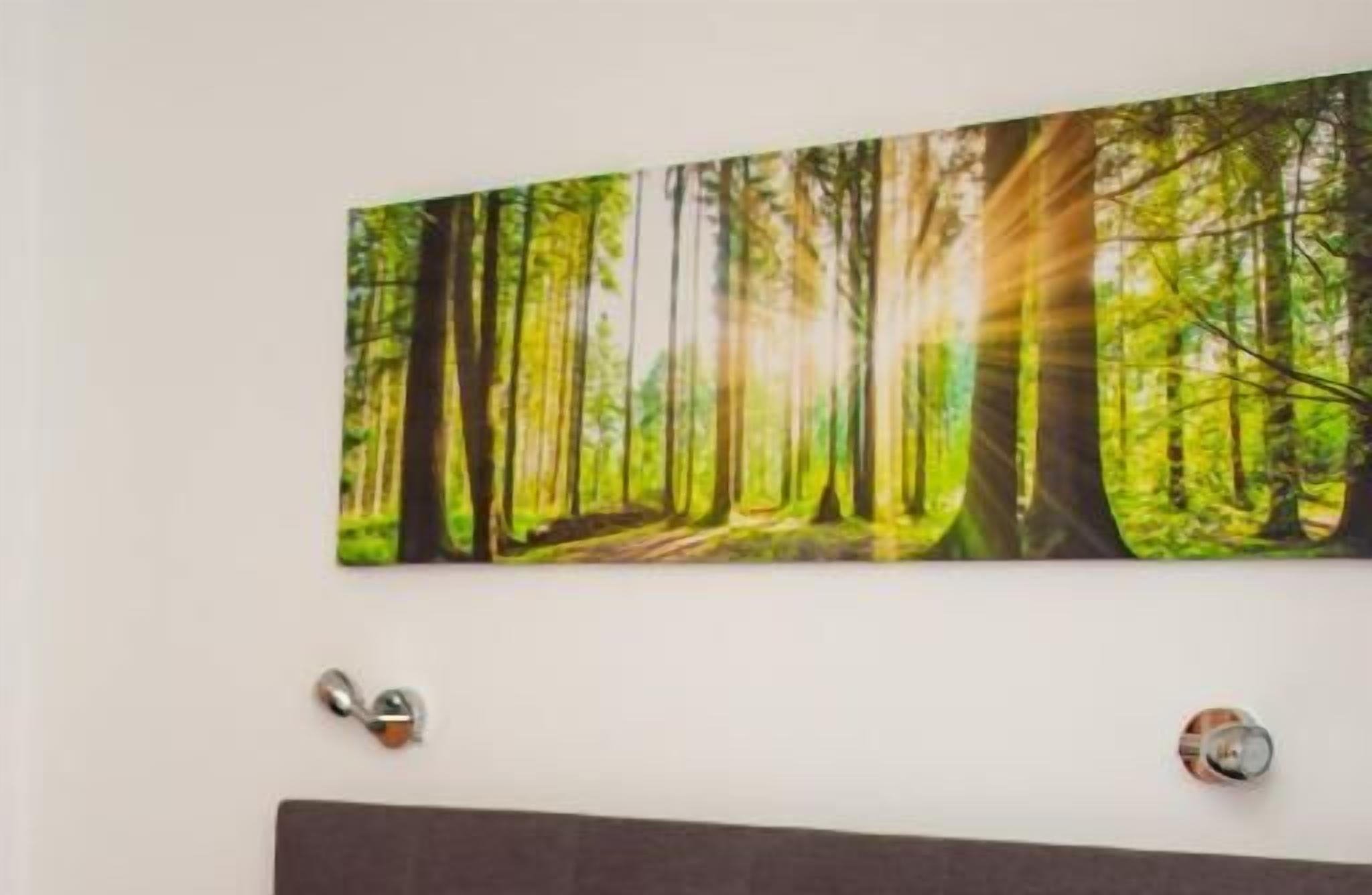 A wall with a forest scene painting, a door handle, and a round object on the wall.