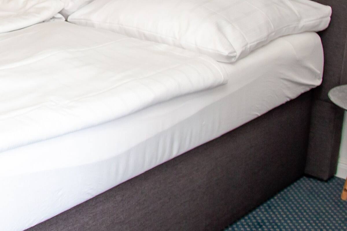 Un lit bien fait, avec du linge de lit blanc et une tête de lit grise.