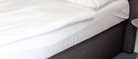A neatly made bed with white linens and a grey headboard.