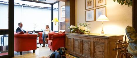Un hall con sillones rojos, un mueble de madera con un reloj y un perro descansando sobre una alfombra estampada.