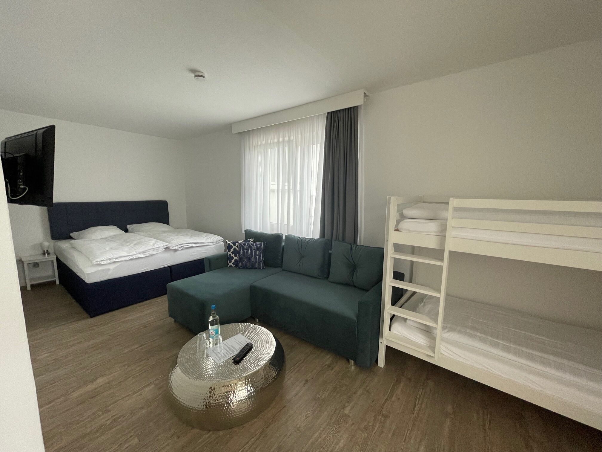 Una habitación de hotel moderna con cama, sofá, literas y una mesa de centro redonda.