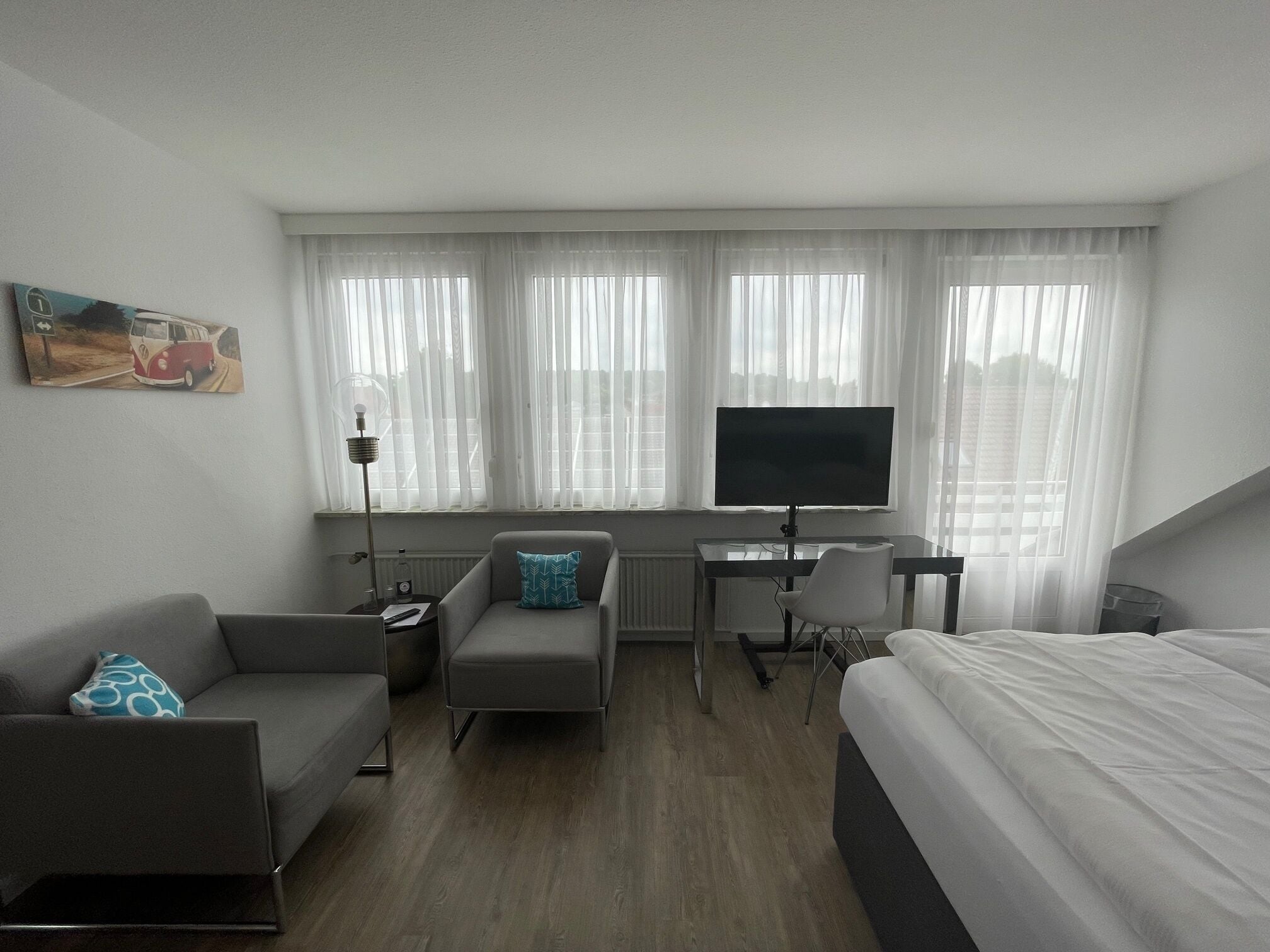 A hotel room with a bed, a desk with a TV, a sofa, and a chair.