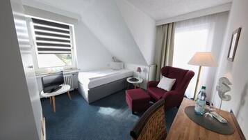 Une chambre d’hôtel de taille réduite, comprenant un lit, un fauteuil rouge, une petite table et un bureau.