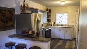 Una cocina con refrigerador, estufa y taburetes de bar.