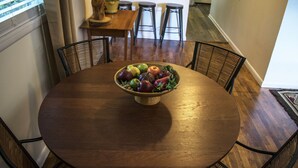 Una mesa de madera redonda con un bol de fruta en el centro, rodeada por cuatro sillas de estructura metálica.