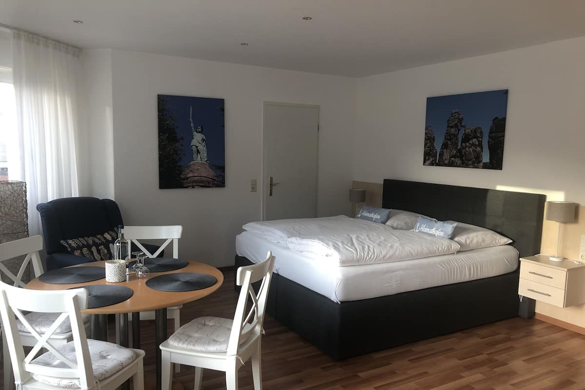 A modern hotel room with a large bed, a dining table with chairs, and two paintings on the walls.
