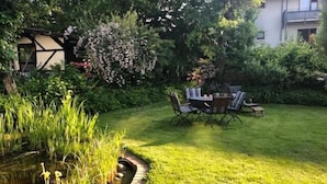 Un jardin bien entretenu avec un étang, un coin repas avec des chaises et une table, et une maison en arrière-plan.