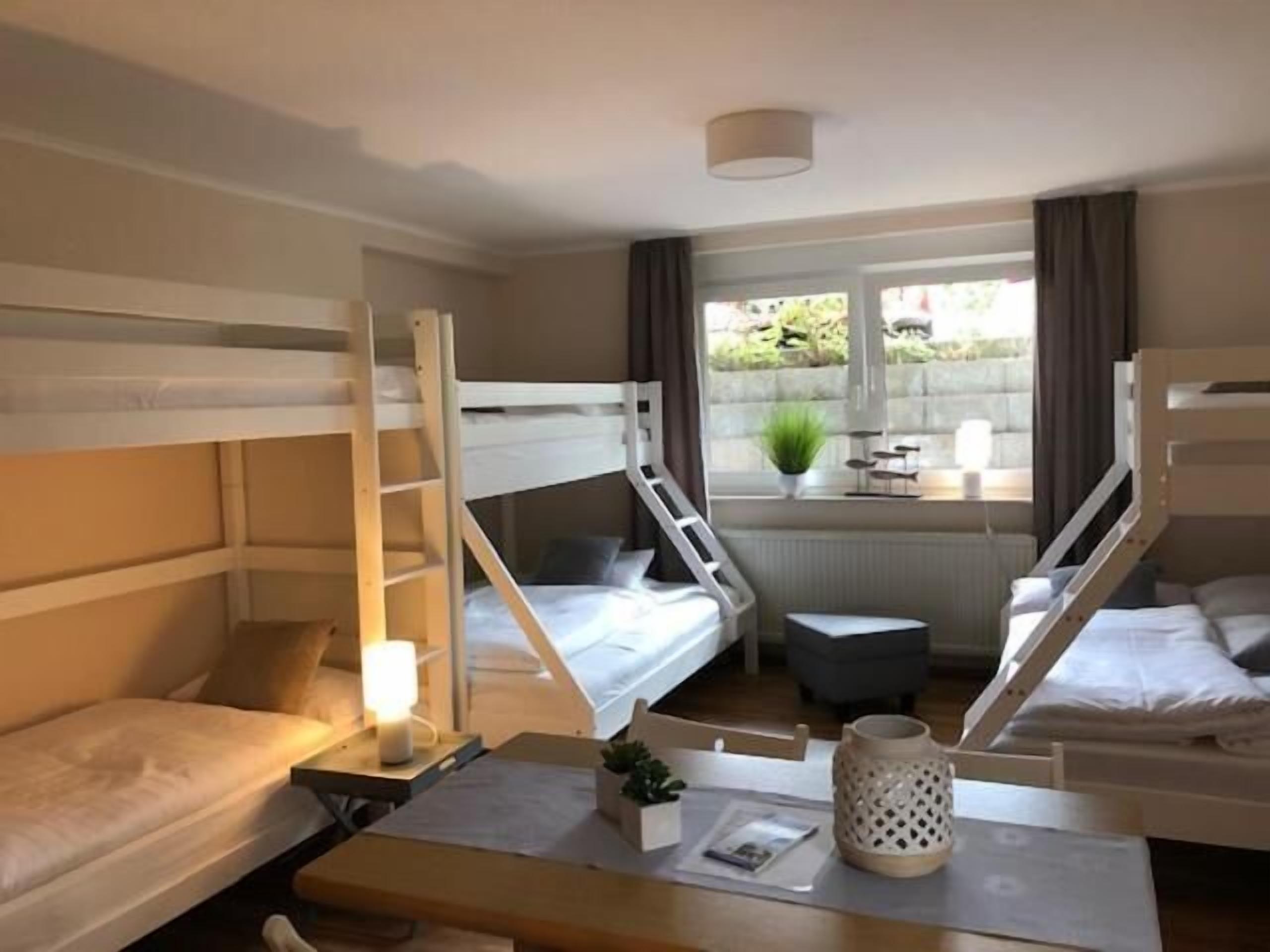 A bunk bed room with a desk, chair, and a small table with a lamp.