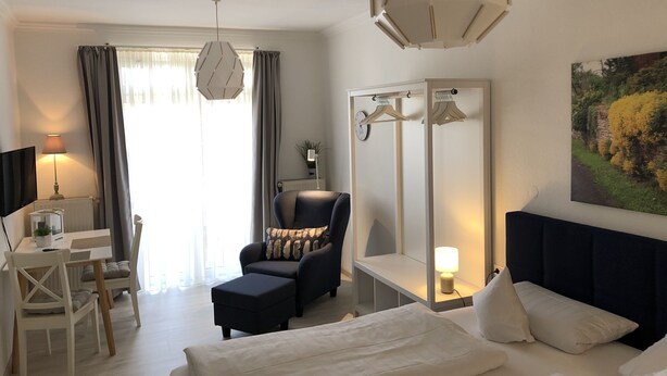 Une chambre d’hôtel avec un lit, un bureau, une chaise, un miroir et un tableau au mur.