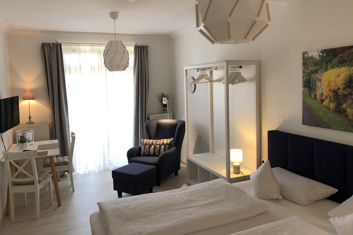 A hotel room with a bed, a desk, a chair, a mirror, and a painting on the wall.
