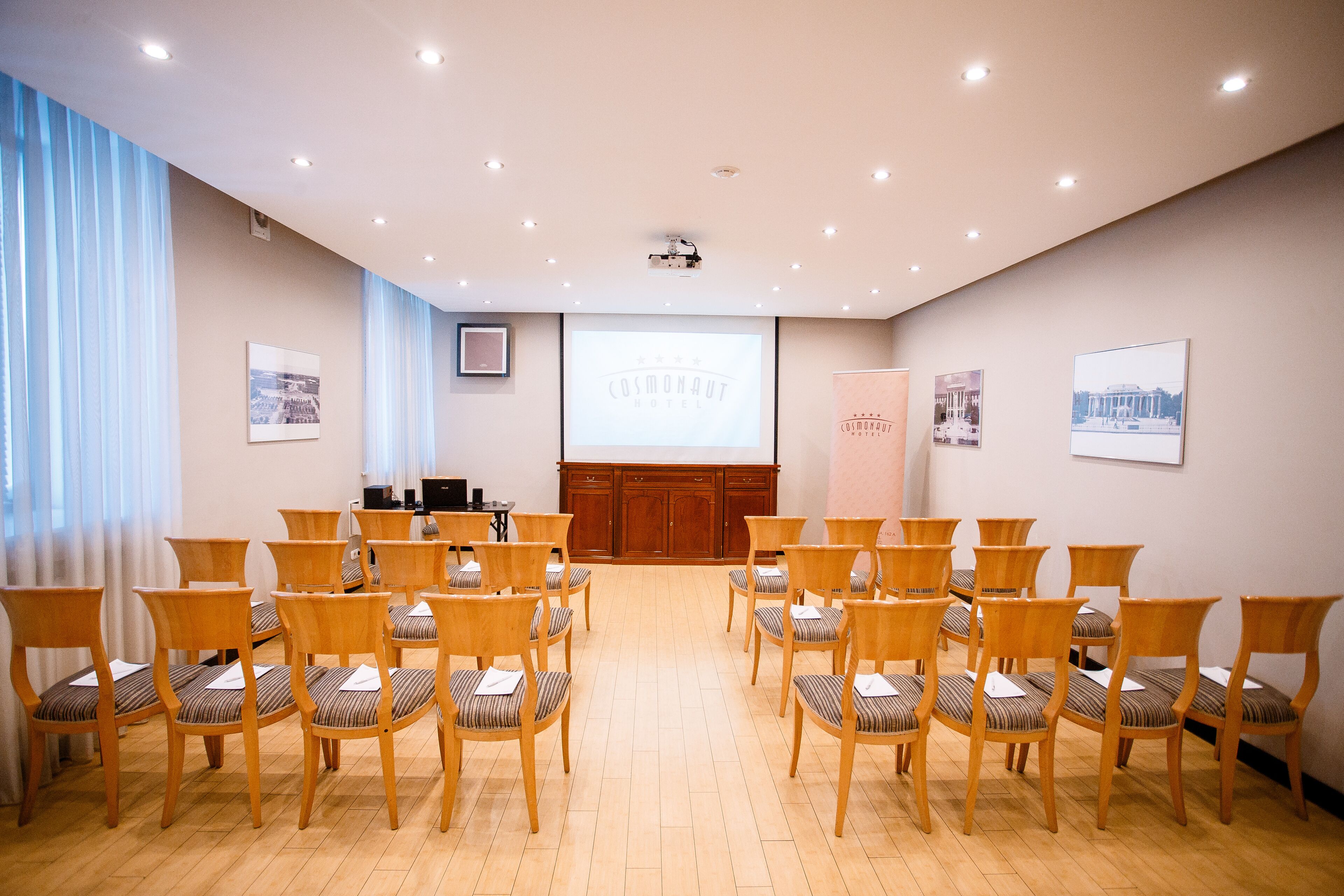 Un salón de conferencias con sillas de madera dispuestas en filas, un atril y una pantalla de proyección que muestra 