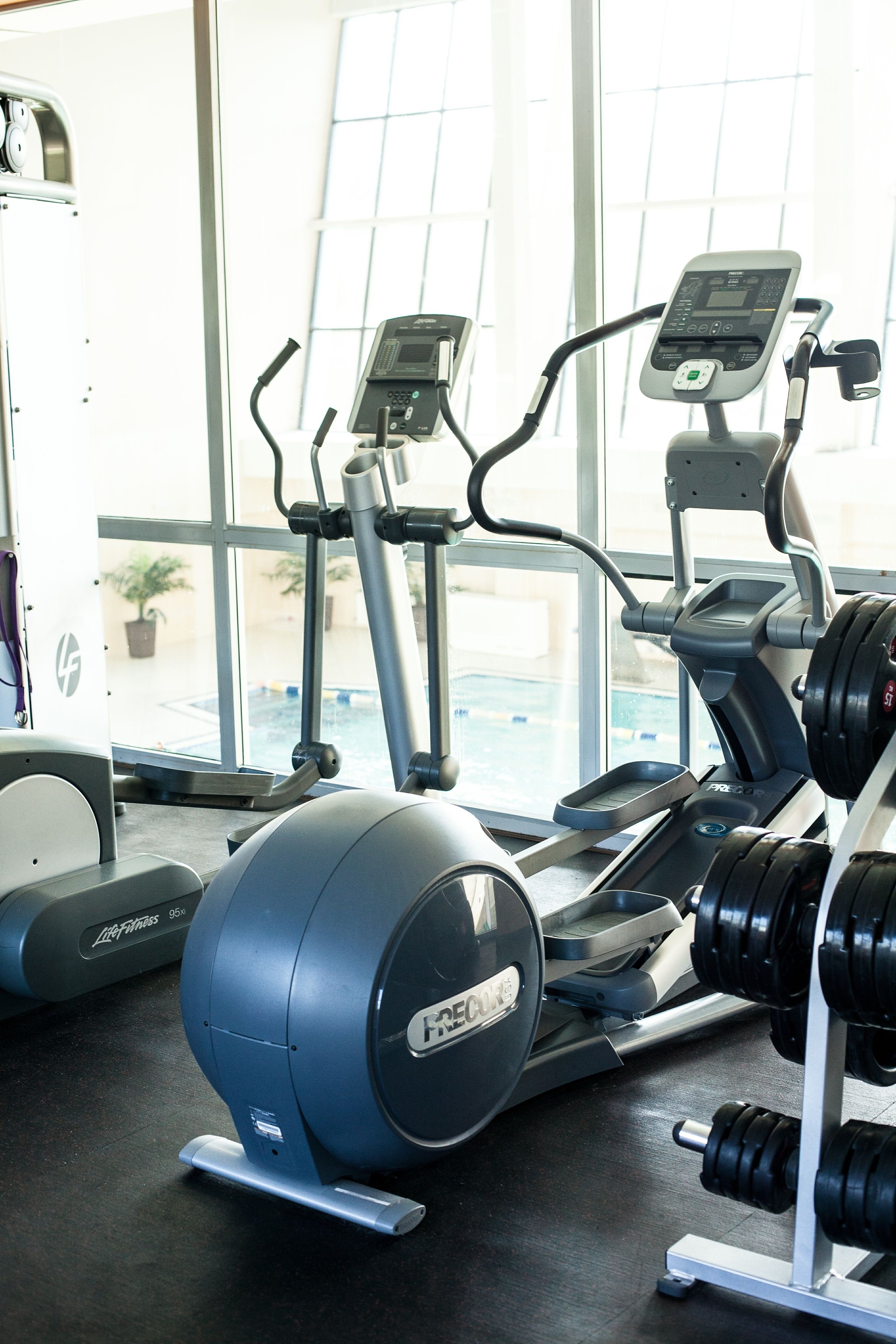 Un gimnasio con equipo de ejercicios, incluyendo cintas de correr, una elíptica y una banca de pesas con mancuernas.
