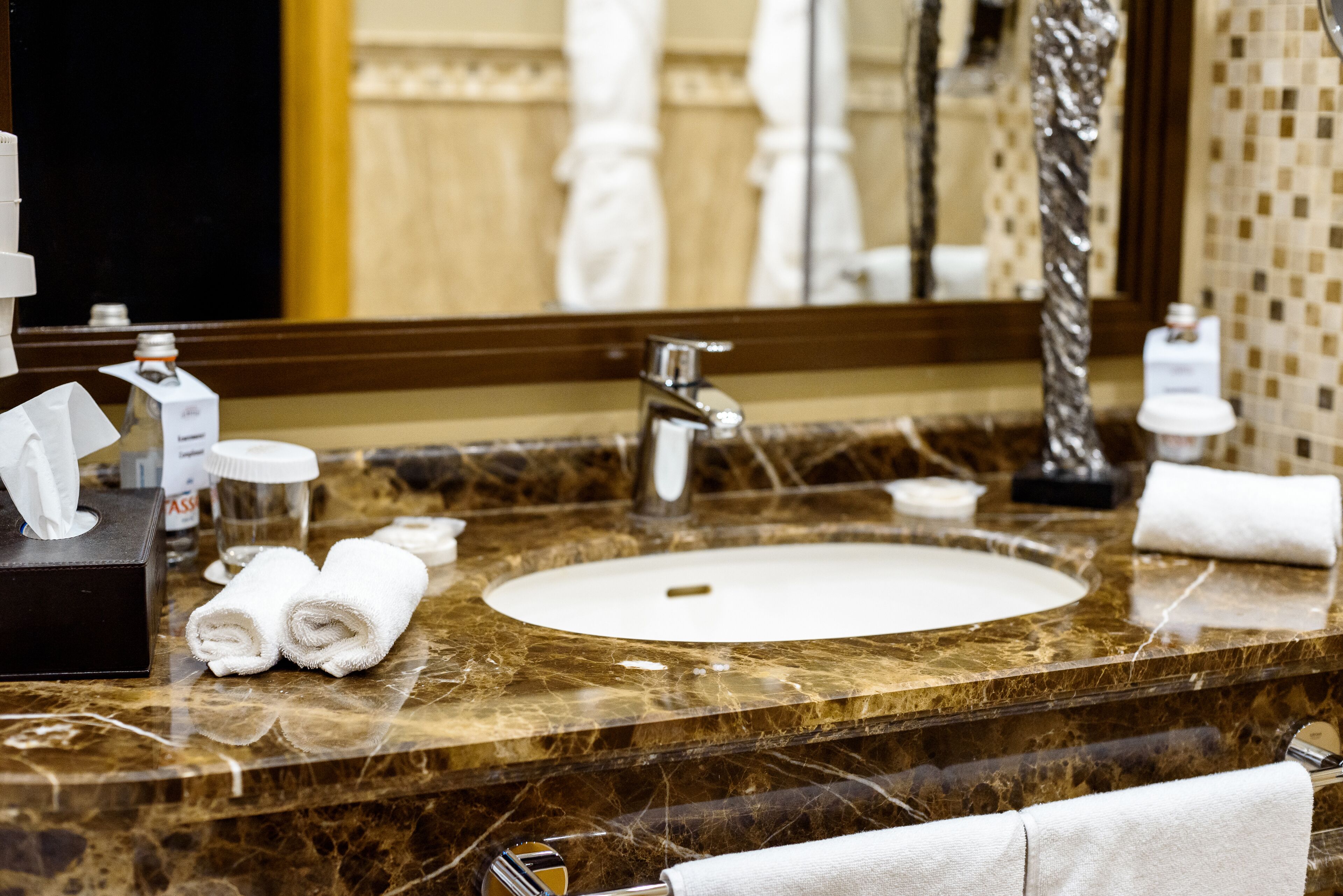 A marble bathroom sink with a mirror, towels, and toiletries.