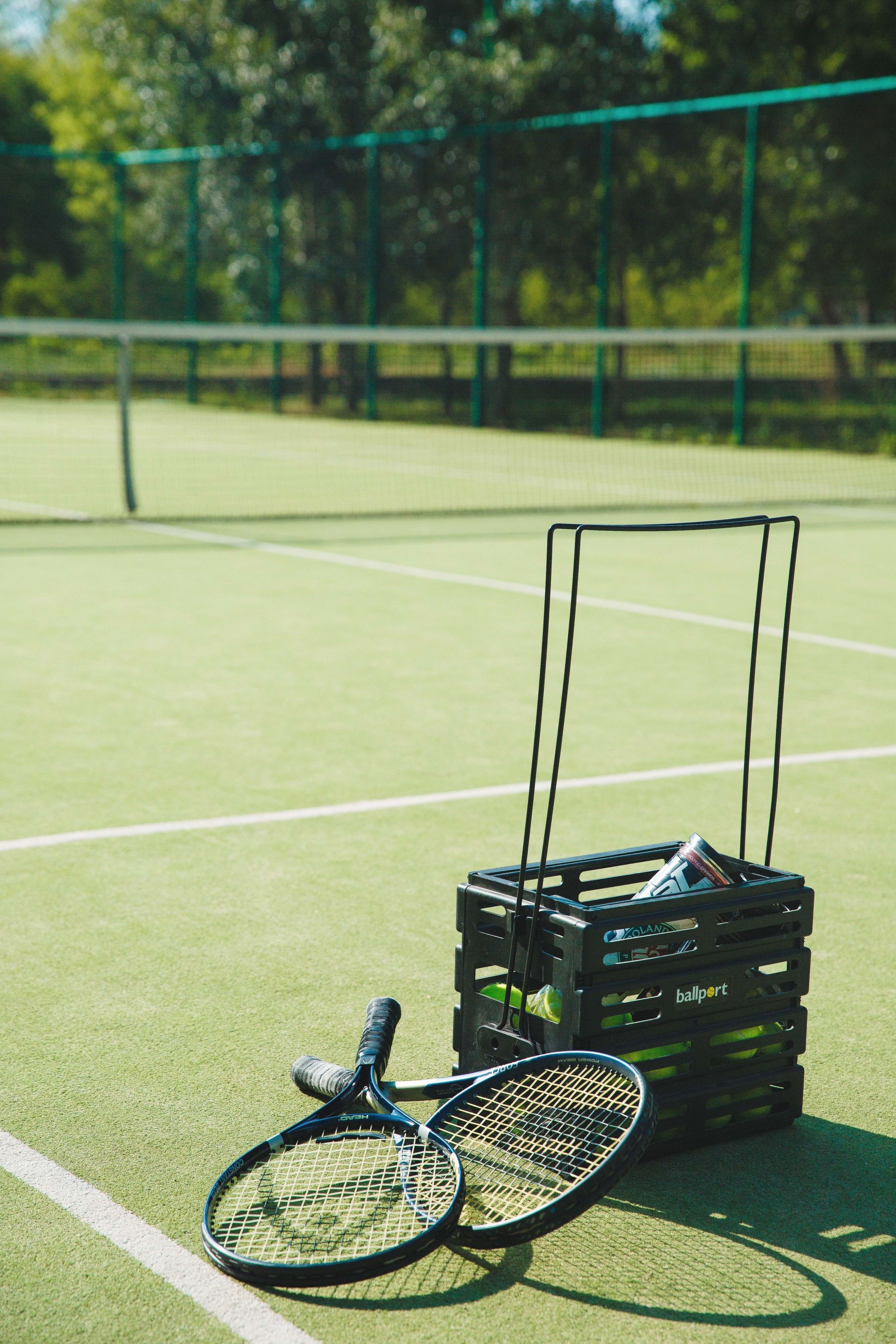 A tennis court with two rackets and a basket of tennis balls.
