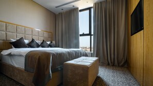 Ett modernt hotellrum med en stor säng, ett träbeklätt sänggavel, en platt-TV och utsikt över staden genom stora fönster.