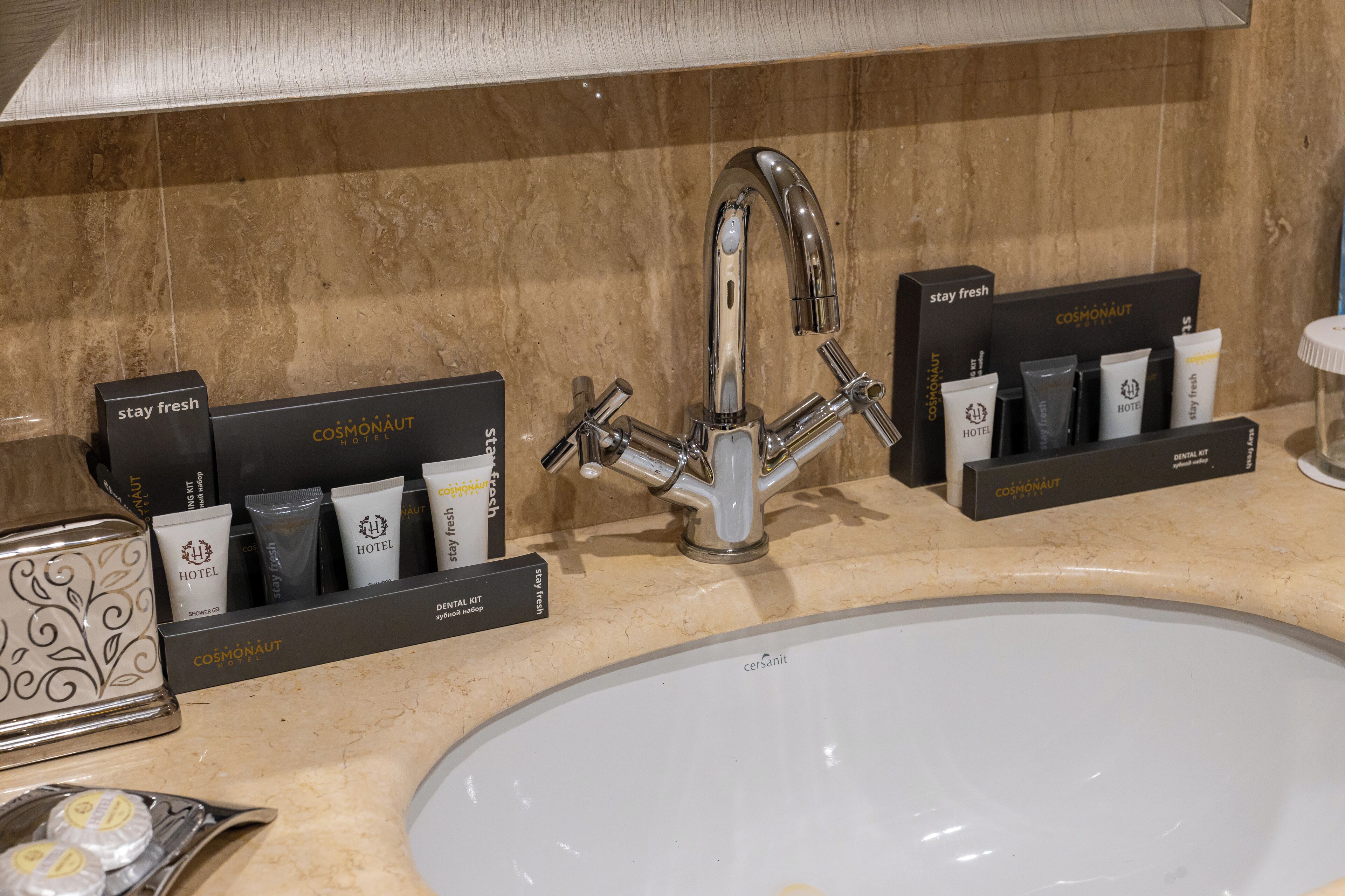 A bathroom sink with a modern faucet, a mirror, and toiletries organized in black boxes labeled "Cosmonaut Hotel."