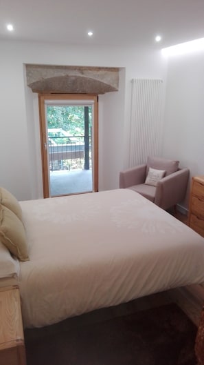 Un dormitorio con una cama grande, una silla, un aparador y vistas al exterior.