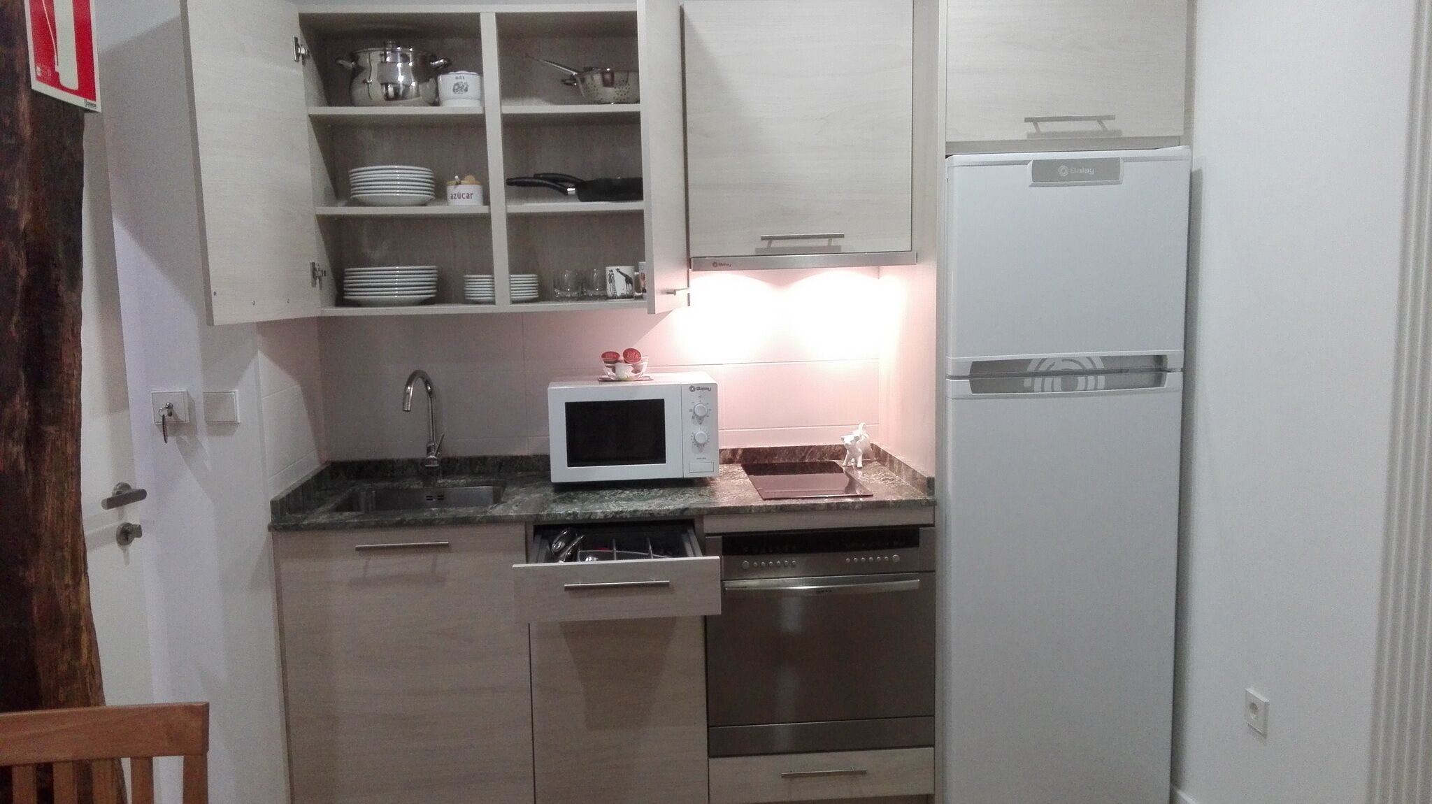 A compact kitchen with white cabinets, a microwave, a refrigerator, and a sink.