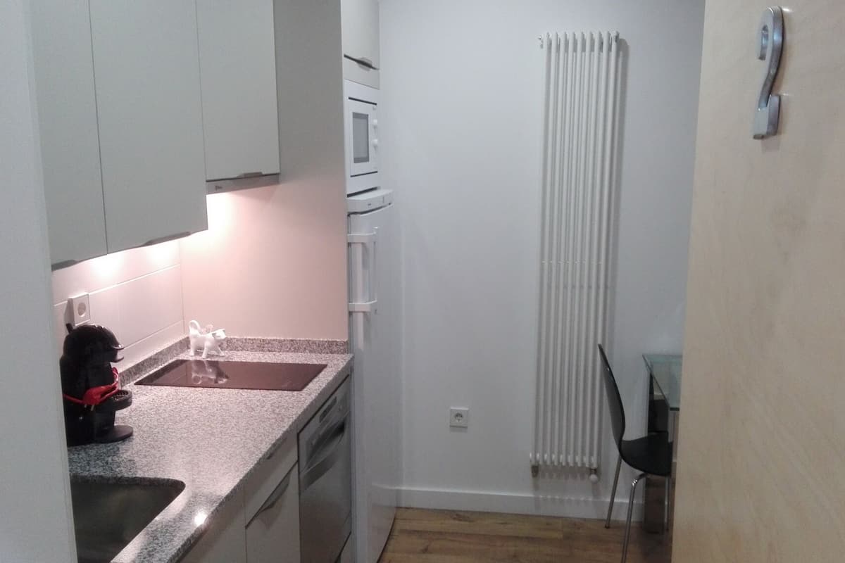 A narrow kitchen with white cabinets, a granite countertop, a small sink, and a white radiator.