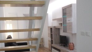 A modern interior with a wooden staircase, a dining area with a glass table, and a kitchen area with a TV and cabinets. - Apartamentos Turísticos Los Picos (Liérganes)