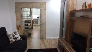 A living room with a black sofa, a patterned throw pillow, a wooden TV stand, and a stone wall. - Apartamentos Turísticos Los Picos (Liérganes)