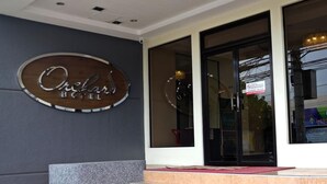 Fachada de un hotel con un letrero de madera que dice "Orchard Hotel". Se ven unos escalones que llevan a la entrada, y una puerta de cristal.