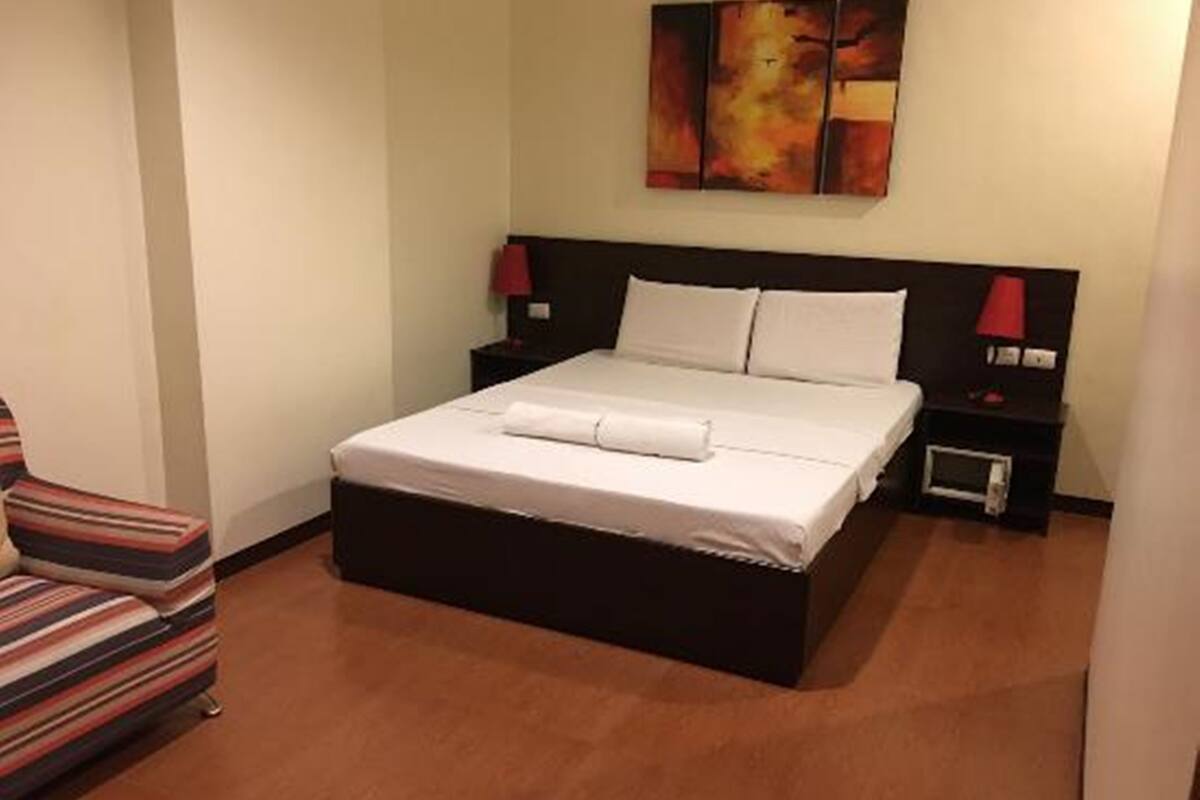 A hotel room with a bed, a nightstand, a chair, and a painting on the wall.