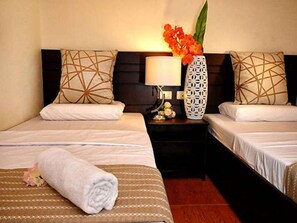 A hotel room with two beds, a nightstand with a lamp, a vase with flowers, and a rolled towel on the bed. - Orchard Hotel (Davao)