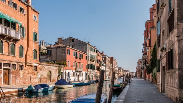A narrow canal in Venice with boats docked along the sides and buildings lining the waterway.