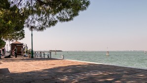 A waterfront promenade with a tiled walkway, a small wooden structure, and a clear view of the water.