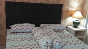 Ein Bett mit einem gemusterten Überwurf, einem dunklen Kopfteil und einer Nachttischlampe auf einem Beistelltisch.