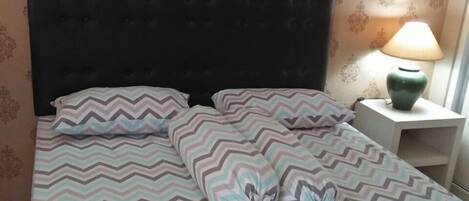 Un lit avec une couvre-lit à motifs, une tête de lit sombre et une lampe de chevet posée sur une table de chevet.