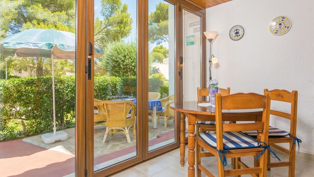 A dining area with wooden chairs and a table, a glass door leading outside, and a ceiling fan. - ENCINAS 1 - Apartment with terrace in Port De Pollença. Free WiFi (Pollença)